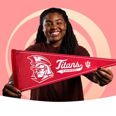A female student holding a Titans banner on a peach background with a light orange swirl behind her