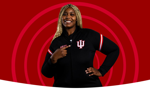A student pointing to the trident on her shirt in front of a radiating circle